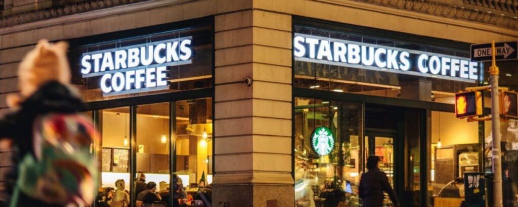 Imagen de un café Starbucks en una mesa junto a una ventana con vista al exterior, rodeado por una taza de café, una cuchara y un libro, que simboliza la experiencia acogedora y de alta calidad que la marca ofrece a sus clientes en todo el mundo.